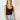 front view of model wearing the Avery Black Sleeveless Bodysuit that has black knit fabric, a scooped neckline, thick straps, and a thong bottom with snap closures.