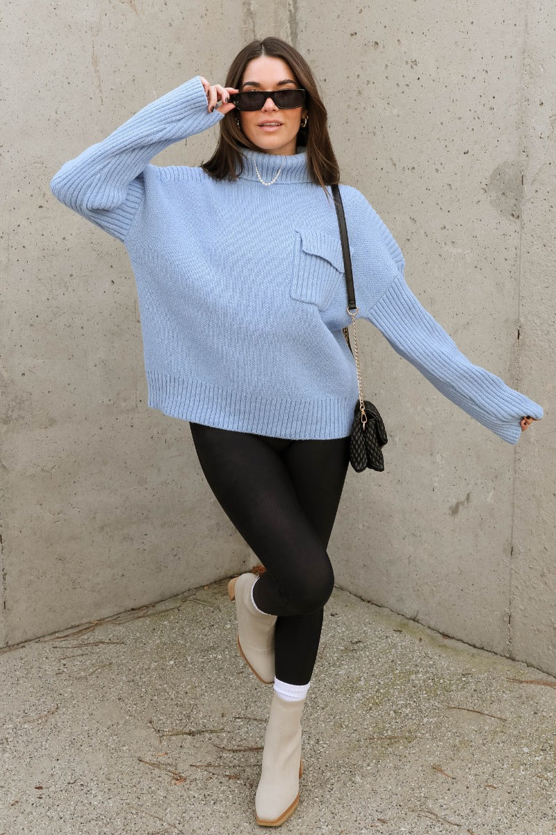 Full body view of model wearing the Grace Light Blue Long Sleeve Sweater which features light blue cable knit fabric, ribbed hem, a ribbed turtleneck neckline, a left front chest folded pocket, dropped shoulders, and long sleeves.