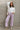 Full body view of model wearing the Emily Lavender Wide Leg Pants which features acid lavender denim-like fabric, two front pockets, a front zipper with a button closure, belt loops, two back pockets, and wide legs.