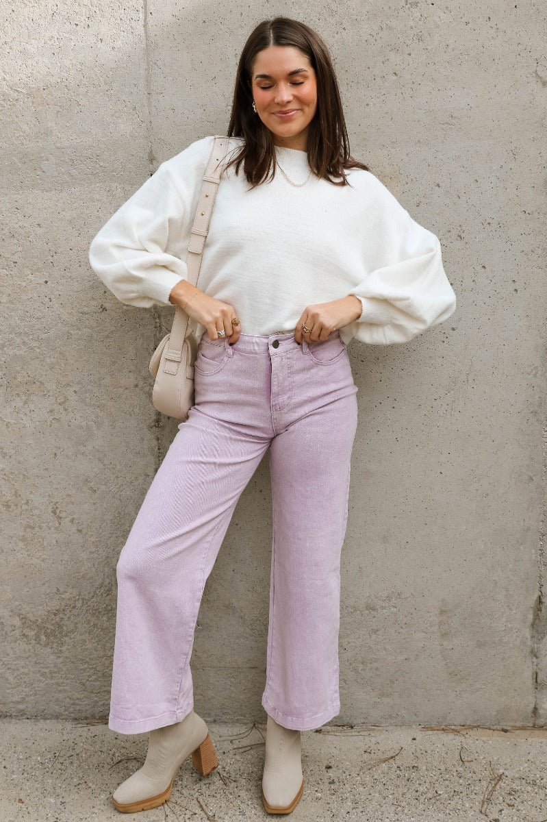 Full body view of model wearing the Emily Lavender Wide Leg Pants which features acid lavender denim-like fabric, two front pockets, a front zipper with a button closure, belt loops, two back pockets, and wide legs.