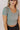 Front view of model wearing the Shae Sage Green One-Size Crop Top that has muted sage ribbed fabric, cropped waist, round neckline and short sleeves.