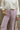 Close up view of model wearing the Emily Lavender Wide Leg Pants which features acid lavender denim-like fabric, two front pockets, a front zipper with a button closure, belt loops, two back pockets, and wide legs.