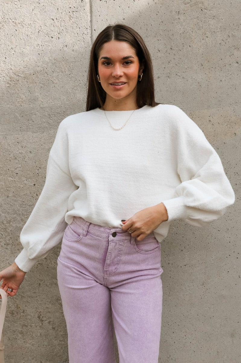 Front view of model wearing the Ella Cream Drawstring Cinch Long Sleeve Sweater which features white knit fabric, a round neckline, dropped shoulders, long balloon sleeves with ribbed cuffs, and a drawstring cinch detail in the back.