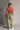 Full body back view of model wearing the Kimberly Olive Wide Leg Cargo Pants that have olive green denim-like fabric, brown contrast stitching, distressing, cargo pockets, a front zipper, belt loops, and wide legs.