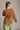 Back view of model wearing the Harlee Camel Open-Knit Sweater which features camel open knit fabric, slits on each side, a round neckline and long wide sleeves.
