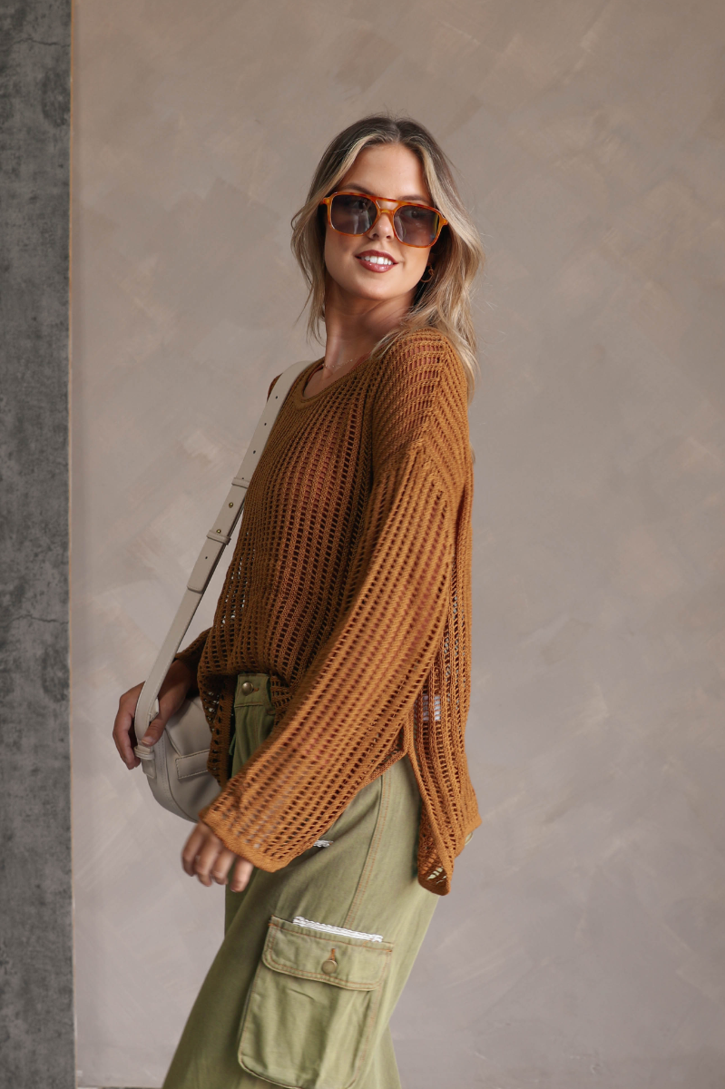 Side view of model wearing the Harlee Camel Open-Knit Sweater which features camel open knit fabric, slits on each side, a round neckline and long wide sleeves.