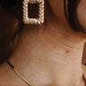 Side view of model wearing the Maliyah Gold Earrings that feature gold metallic roped open rectangles with studs attached.