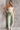 Full body view of model wearing the Alexa Sage High-Waisted Wide Leg Pants which features sage denim fabric, two front pockets, two back pockets, front zipper with button closure, belt loops and wide pant legs.