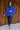Full body front view of model wearing the Maren Blue Teddy Jacket that has royal blue faux-fur sherpa fabric, tortoise buttons, pockets, a collar, and long sleeves with buttoned cuffs.