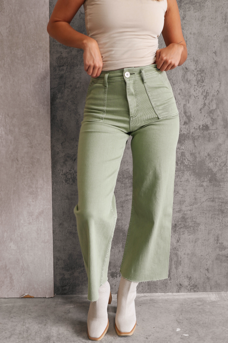 Front view of model wearing the Alexa Sage High-Waisted Wide Leg Pants which features sage denim fabric, two front pockets, two back pockets, front zipper with button closure, belt loops and wide pant legs.