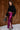 Full body side view of model wearing the Lainey Magenta Slit Midi Skirt which features fuchsia and black shimmer pleated fabric, midi length, slit on the side, thigh length fuchsia lining and elastic waistband.