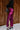 Full body side view of model wearing the Lainey Magenta Slit Midi Skirt which features fuchsia and black shimmer pleated fabric, midi length, slit on the side, thigh length fuchsia lining and elastic waistband.