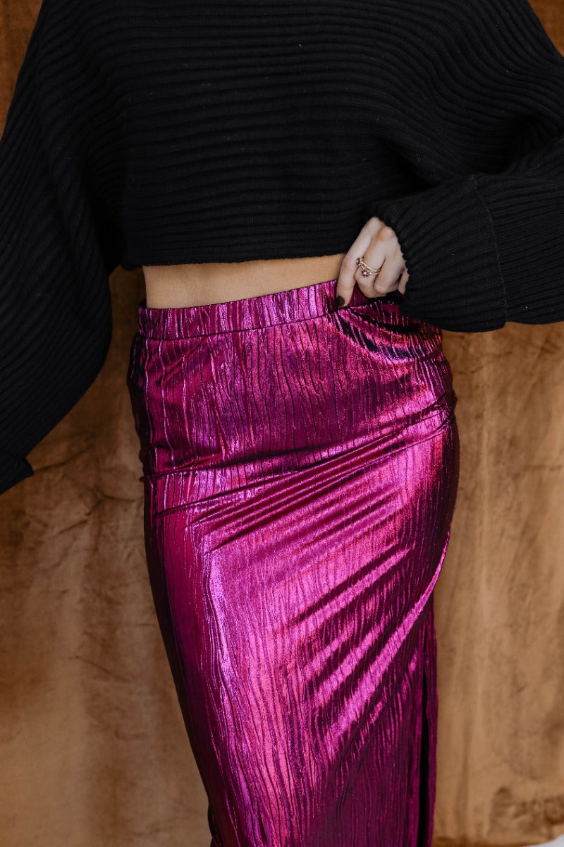 Front view of model wearing the Lainey Magenta Slit Midi Skirt which features fuchsia and black shimmer pleated fabric, midi length, slit on the side, thigh length fuchsia lining and elastic waistband.