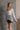 Frontal view of model wearing the Sahara Grey Crochet Knit Long Sleeve Sweater that has grey open knit fabric, a high-low hem, slits on each side, a round neckline and long flare sleeves.