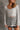 Close front view of model wearing the Sahara Grey Crochet Knit Long Sleeve Sweater that has grey open knit fabric, a high-low hem, slits on each side, a round neckline and long flare sleeves.