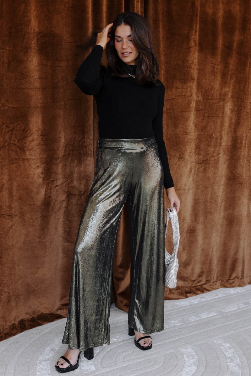 Full body view of model wearing the Haven Gold & Black Flare Pants which features black and gold shimmer fabric, high waistline and flare pant legs.