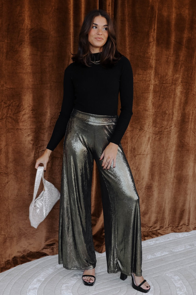Full body view of model wearing the Haven Gold & Black Flare Pants which features black and gold shimmer fabric, high waistline and flare pant legs.