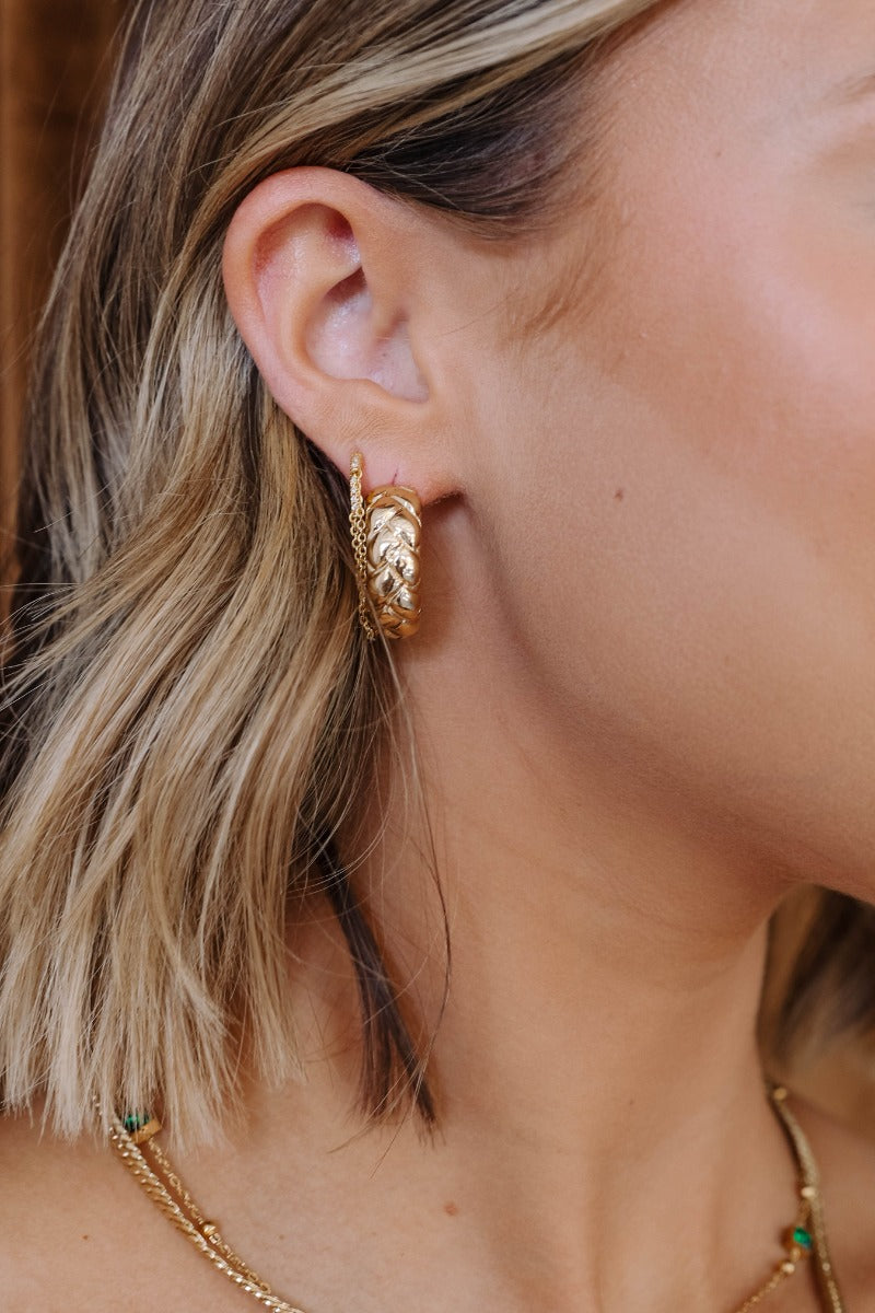 Side view of model wearing the Leona Braided Gold Hoop Earrings that has open, shiny, gold hoops with a braided pattern design.