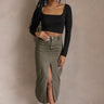 Full body front view of model wearing the Kara Olive Denim Front Slit Midi Skirt that has olive green denim fabric, midi length, a front slit, a front zipper with a button closure, and belt loops.