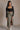 Full body front view of model wearing the Greta Black Basic Long Sleeve Crop Top that has black knit fabric, a cropped waist, a thick band hem, a square neckline, and long sleeves.
