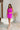 Full body front view of model wearing the Don't Be Shy Dress , which features a purple material, a halter neck with a tie, pleat details on the straps, an open back, and a back zipper closure.