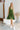 Frontal view of the Falling Flowers Dress that features a moss green material, a deep V neckline, a sleeveless design with thick straps, a side ruffle detail, a lettuce edge bottom hem, a V back, a flowy fit, and a mini length