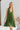 Frontal view of the Falling Flowers Dress that features a moss green material, a deep V neckline, a sleeveless design with thick straps, a side ruffle detail, a lettuce edge bottom hem, a V back, a flowy fit, and a mini length