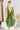 Back view of the Falling Flowers Dress that features a moss green material, a deep V neckline, a sleeveless design with thick straps, a side ruffle detail, a lettuce edge bottom hem, a V back, a flowy fit, and a mini length