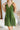 Frontal view of the Falling Flowers Dress that features a moss green material, a deep V neckline, a sleeveless design with thick straps, a side ruffle detail, a lettuce edge bottom hem, a V back, a flowy fit, and a mini length