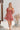 Frontal view of the Mystic Meadows Dress that features a light clay material, a scoop neckline with a tie detail, a half sleeve, a ruched elastic waist, a two-tiered bottom with a ruffle hem, a squared back, and a mini length.