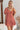Frontal view of the Mystic Meadows Dress that features a light clay material, a scoop neckline with a tie detail, a half sleeve, a ruched elastic waist, a two-tiered bottom with a ruffle hem, a squared back, and a mini length.