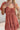 Frontal view of the Mystic Meadows Dress that features a light clay material, a scoop neckline with a tie detail, a half sleeve, a ruched elastic waist, a two-tiered bottom with a ruffle hem, a squared back, and a mini length.