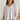 Frontal view of the Silver Lining Top that features a silver material, a collar with a V neckline, a button-up front, a flowy half sleeve, pleats through out, and a flowy fit.