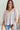 Frontal view of the Silver Lining Top that features a silver material, a collar with a V neckline, a button-up front, a flowy half sleeve, pleats through out, and a flowy fit.