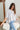 Frontal view of the Silver Lining Top that features a silver material, a collar with a V neckline, a button-up front, a flowy half sleeve, pleats through out, and a flowy fit.