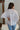 Back view of the Silver Lining Top that features a silver material, a collar with a V neckline, a button-up front, a flowy half sleeve, pleats through out, and a flowy fit.