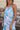 Close front view of model wearing the Bahama Blues Floral Dress that has blue fabric with a pink, light blue, light pink and tan floral pattern, mini length, a halter neck, a sleeveless design, and a back keyhole with a tie closure.