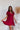 Frontal view of the All Things Nice Dress that features a red colored material, a V neckline, a short flowy sleeve, three buttons below the bust, an elastic waist, a V back with a tie closure, and a flowy fit.