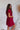 Side view of the All Things Nice Dress that features a red colored material, a V neckline, a short flowy sleeve, three buttons below the bust, an elastic waist, a V back with a tie closure, and a flowy fit.