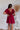 Back view of the All Things Nice Dress that features a red colored material, a V neckline, a short flowy sleeve, three buttons below the bust, an elastic waist, a V back with a tie closure, and a flowy fit.