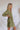 Side view of the Wish You Well Dress that features an olive gauze material, a frayed V neckline, a 3/4 sleeve, a button-up front, a tiered babydoll design, a flowy fit, and a mini length. 