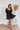 
Frontal view of the Balanced Out Dress that features a black cotton material, a squared neckline, a half sleeve, a tiered babydoll design, a back button closure, a flowy fit, and a mini length.
