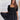 Frontal view of the Balanced Out Dress that features a black cotton material, a squared neckline, a half sleeve, a tiered babydoll design, a back button closure, a flowy fit, and a mini length.