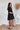 
Side view of the Balanced Out Dress that features a black cotton material, a squared neckline, a half sleeve, a tiered babydoll design, a back button closure, a flowy fit, and a mini length.
