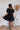 
Back view of the Balanced Out Dress that features a black cotton material, a squared neckline, a half sleeve, a tiered babydoll design, a back button closure, a flowy fit, and a mini length.
