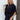 Frontal view of the City Escape Romper that features a black silky material, a rounded neckline, a flowy half sleeve, an elastic wast, a shorts bottom, side cut-outs, an open three tie back, and a flowy fit.