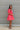 Side view of the Bubble Gum Mini Dress that features a pink cotton material, a squared neckline, a half sleeve, a tiered babydoll design, a back button closure, a flowy fit, and a mini length.