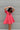 Frontal view of the Bubble Gum Mini Dress that features a pink cotton material, a squared neckline, a half sleeve, a tiered babydoll design, a back button closure, a flowy fit, and a mini length.