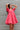 Frontal view of the Bubble Gum Mini Dress that features a pink cotton material, a squared neckline, a half sleeve, a tiered babydoll design, a back button closure, a flowy fit, and a mini length.