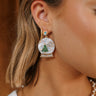 Side view of model wearing the Snow Globe Earrings that have dangle snow globes with a snowflake and christmas tree in irredescent, clear, and green stones. 